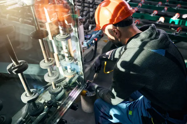 Specialist works in the production of double-glazed windows with high-tech equipment, a man wearing protective gloves