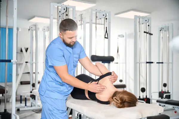 Chiropractor works with a patient in a rehabilitation center, a woman in a comfortable training suit