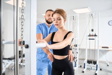 Kadın hasta, özel bir cihaz kullanarak bir uzmanın gözetiminde kineziyoloji kliniğinde tutuluyor.