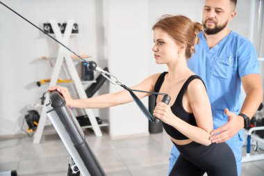 Erkek fizyoterapist, özel bir simülatörde kadın bir hastayla çalışıyor. Kliniğin modern ekipmanları var.