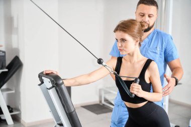 Fizyoterapist hastayla özel bir simülatörde çalışıyor. Kliniğin modern ekipmanları var.