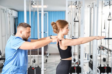 Kinezyolog genç bir hastanın egzersizlerini izler, spor salonunda dersler düzenlenir.