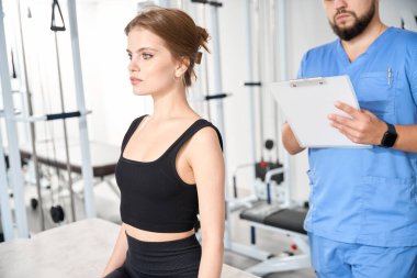 Kinezyolog genç bir bayanla görüşüyor, danışmanlık spor salonunda yapılıyor.