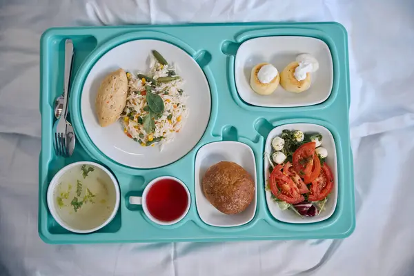 Top view of plastic food tray placed on bed with clean white sheet in hospital room
