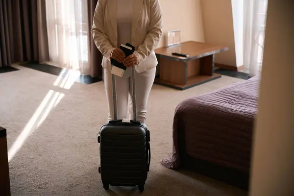 带着旅行证件和手提箱站在酒店房间中央的照片 图库照片