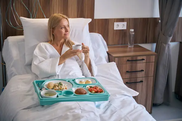 Paciente Pensativo Sentado Cama Hospital Com Bandeja Alimentos Segurando Xícara Imagem De Stock