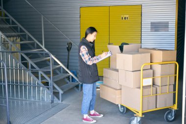 Karton kutularla dolu bir platform vagonunda beklerken panoya kalemle yazan depo çalışanının yan görünümü