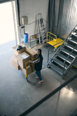 Gülümseyen nakliye aracının en üst görüntüsü depo binasının çıkış kapısına doğru kutularla dolu.