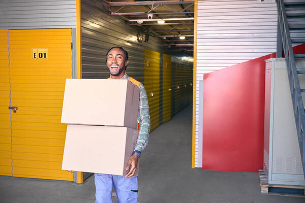 Merry loader holding cardboard boxes in hands while standing in front of cargo containers in storage area