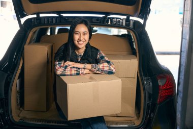 Depoda bir arabanın bagajında otururken elinde karton bir kutu tutan çekici bir kadın.