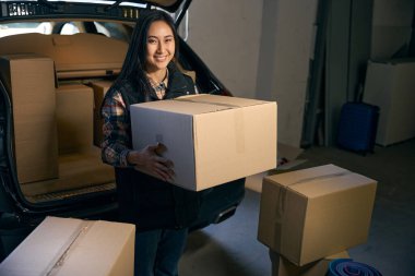 Genç bayan, bir deponun bagajında otururken elinde bir kutu tutuyor.