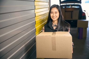 Depoda elinde bir kutu tutan gülümseyen kadın. Kapat.