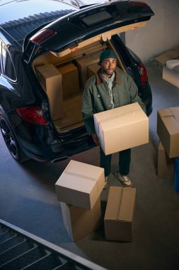 Genç bir erkek, bir arabanın bagajında depolama hizmeti veren karton kutuları boşaltıyor. Üst görünüm
