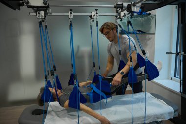 Erkek rehabilitasyon uzmanı, modern ekipmanlar kullanarak hastayı askıya aldı.