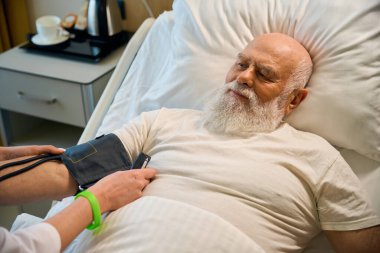 Kadın bir doktor kan basıncını ölçerken hasta hastane yatağında yatıyor.