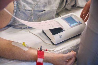 Yetişkin doktor hastane yatağında eski bir hastanın kardiyogramını ölçüyor.