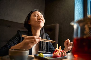 Heyecanlı Asyalı kadın lezzetli suşi setini karides ve tobiko yumurtası ile yiyor zevk ve zevkle, her rulo ekmeğin tadını çıkarıyor, sıcak restoranda en sevdiği yemeği servis ediyor.