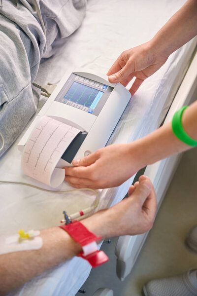 Кавказская женщина-врач измеряет кардиограмму пациента, лежащего на кровати