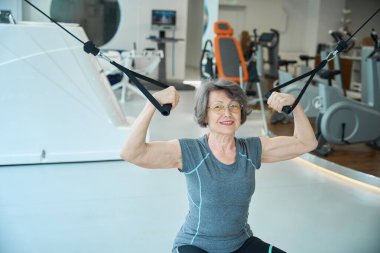 Yaşlı bayan spor salonundaki bir makinede çalışıyor. Rahat spor kıyafetleri içinde bir kadın.
