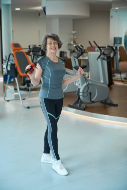 Yaşlı bir kadın spor salonunda ip atlarken rahat bir şekilde idman yapıyor.