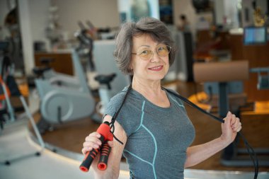 Yaşlı bayan atlama halatıyla özel tatbikatlar yapıyor. Rahat spor kıyafetleri giymiş bir kadın.