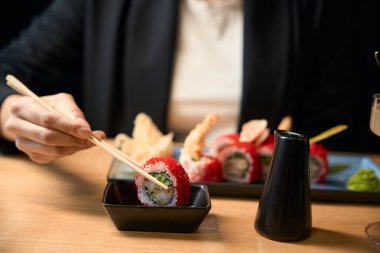 Lezzetli taze suşi yiyen karidesli ve çubuklu tobiko yumurtası yiyen, suşiyi soya sosuna batıran, Asya mutfağında iş yemeği yiyen bir kadın.