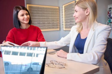 Yönetici, kadın bir müşteriyle göz teması kuruyor. Masada bir sürü numune var.