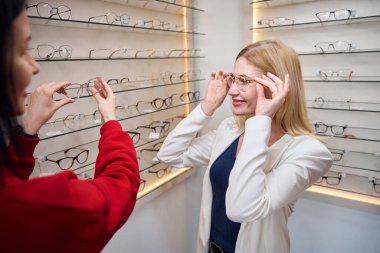 Gözlük mağazası müdürü güzel bir sarışın için gözlük seçiyor. Vitrinde bir sürü örnek var.