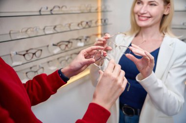 Bir gözlük mağazasının yöneticisi bir müşteriye çerçeve seçiminde yardımcı olur, görüntüde çok sayıda örnek vardır