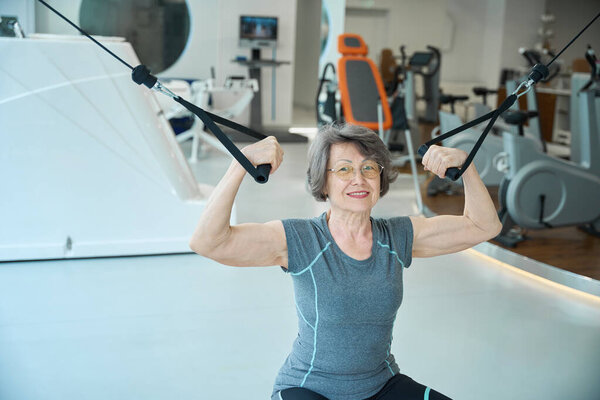 Elderly lady is working out on a machine in a gym, a woman in comfortable workout clothes