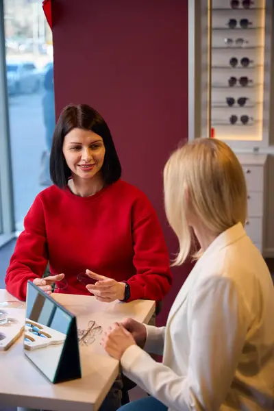 stock image Female consultant communicates with a client in an eyewear store, there are many samples on the table