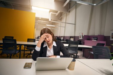 Çalışan bir dizüstü bilgisayarın önünde kafasını tutan beyaz bir kadın.