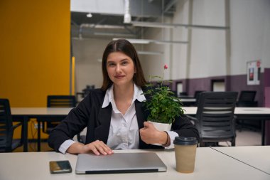 Genç bayan masasında oturuyor ve elinde bir saksıda çiçek tutuyor.