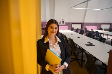 Elinde çantaları olan genç bir kadın kameraya bakar ve gülümser.