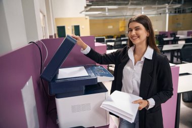 Genç bir kadın belgeleri kopyalıyor ve gülümseyen kameraya bakıyor.