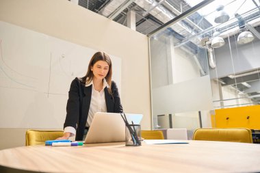 Genç esmer kız geniş bir ofis odasında tahtaya yazı yazıyor.