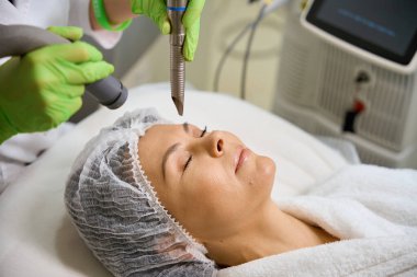 Donanım kozmetoloji prosedürü sırasında koruyucu şapkalı bir kadın koruyucu eldivenlerle çalışır.