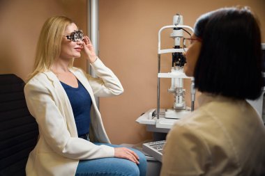 Genç sarışın kadın deneme lenslerini deniyor, doktor özel bir cihaz kullanıyor.