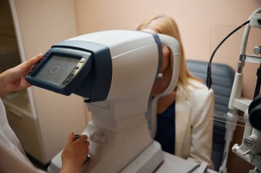 Bir göz doktoruyla randevusu olan genç bir kadın, doktor hastaların gözlerini muayene eder.