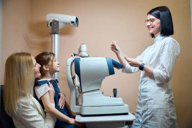 Anne ve küçük kızı otomatik fraktometrenin başında oturuyorlar. Bir göz doktoruna danışıyorlar.