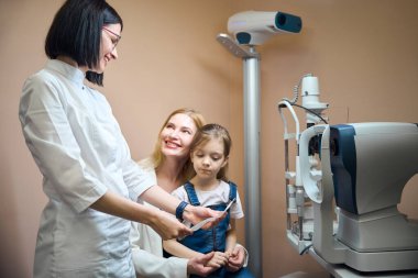 Kadın göz doktoru genç bir hastanın annesiyle iletişim kurar, doktor bir reçete yazar.