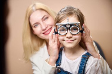 Gözlüklü küçük bir hasta, annesiyle göz doktoruyla randevusu olan bir kız.
