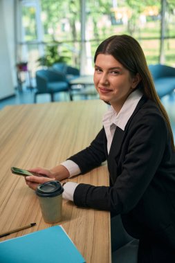 Genç bayan çalışan kameraya bakıp gülümsüyor ve telefonu tutuyor.