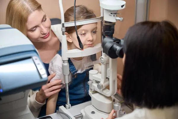 Stock image Doctor uses modern equipment to check the vision of a young patient, the girl is supported by her mother