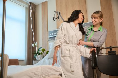 Hemşire, klinikteki hastaya yataktan tekerlekli sandalyeye nakledilmesinde yardımcı olur.