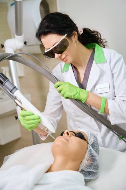 Dermatolog, modern ekipmanlar kullanan orta yaşlı bir hastanın yüzüyle çalışıyor.