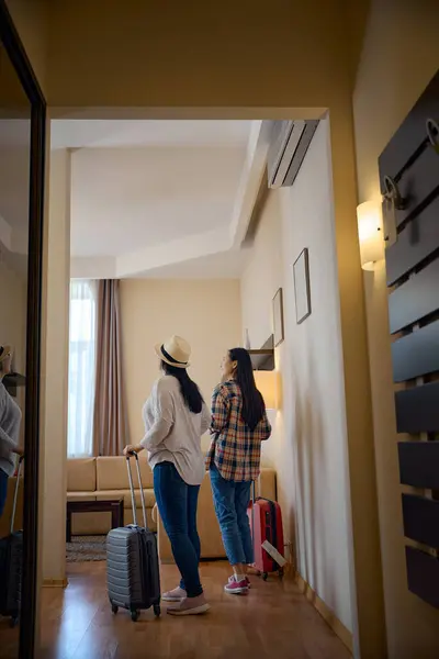 stock image Back view of smiling young Asian woman and her female travel companion standing in middle of hotel room