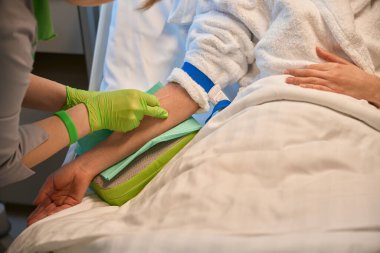 Koruyucu eldivenli hemşire hastaya serum takar, kadın özel bir yatağa oturur.