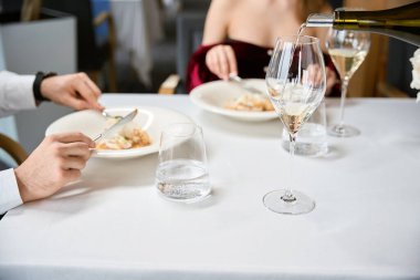 Restoranda flört eden kadın ve erkekler için beyaz şarap bardaklarına beyaz şarap dolduran garsonun kesilmiş fotoğrafı. Romantizm, tarih, ilişki kavramı