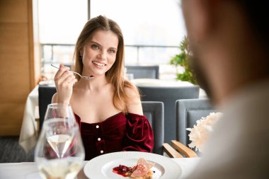 Elinde tatlı kaşığı olan mutlu, genç bir bayan restoranda flört eden bir adama bakıyor. Romantizm, tarih, ilişki kavramı